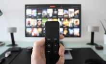 hand holding remote control pointing at tv screen with movie and tv show options