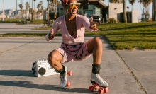 Person crouching and posing on roller skates with boombox behind them.