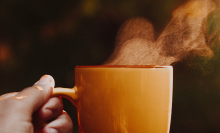 Steam rising from orange mug held by hand