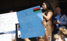 A person holds up a blue protest sign that reads, "Black history is American history."
