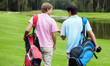 A man in a pink shirt walking on a golf course with a man in a blue shirt
