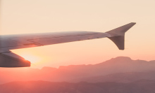 picture of an airplane wing, from the point of view of sitting in the window seat of an aircraft, the sun is going down and the sky is salmon