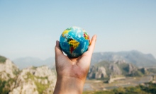A hand holds a miniature globe in front of mountains.