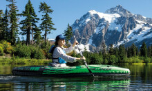 Person navigating a lake with nearby mountains on an inflatable kayak