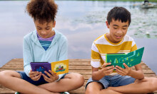 Two kids reading from a Kindle Paperwhite Kids e-reader while sitting on a dock