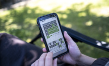 Woman plays Wordle on her smartphone from a seat in a garden