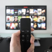 hand holding remote control pointing at tv screen with movie and tv show options