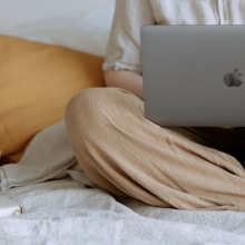Person sitting on a bed on their laptop.
