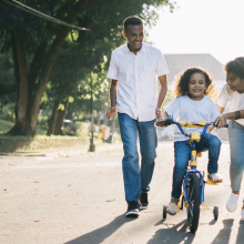 parents teaching kid how to ride a bike in the street
