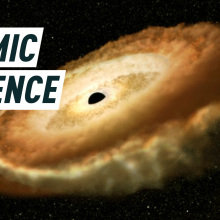 A bright donut-shaped circle of light surrounds a black hole. Caption reads: Cosmic violence.