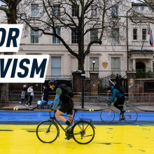 A cyclist passes over a giant Ukrainian flag painted over the Russian Embassy in London. Caption reads: Colored Activism