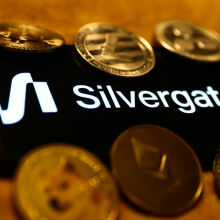 Silvergate logo displayed on a phone screen, surrounded by coins representing cryptocurrencies.