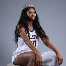 Angel Reese sits for a portrait while wearing white and purple LSU jersey and a crown 