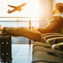 man sitting at airport gate watching a plane take off from the window 