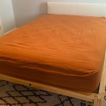 Mattress with burnt orange sheets atop a wood platform bed frame with white pillow board