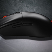 Black MOJO M2 wireless mouse resting lengthwise on a reflecting, gray surface.