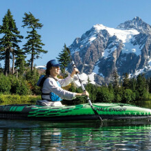 Person navigating a lake with nearby mountains on an inflatable kayak
