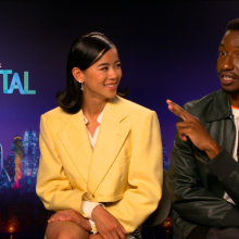 Sat against a purple  'Elemental' backdrop, Leah Lewis smiles at co-star Mamoudou Athie as he gesticulates