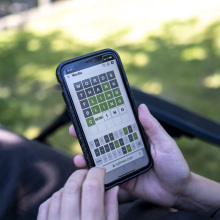 Woman plays Wordle on her smartphone from a seat in a garden