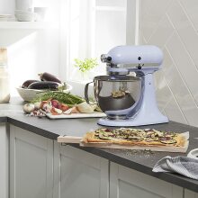 The baby blue KitchenAid Artisan Series 5-Quart stand mixer on a kitchen countertop surrounded by a vast variety of ingredients