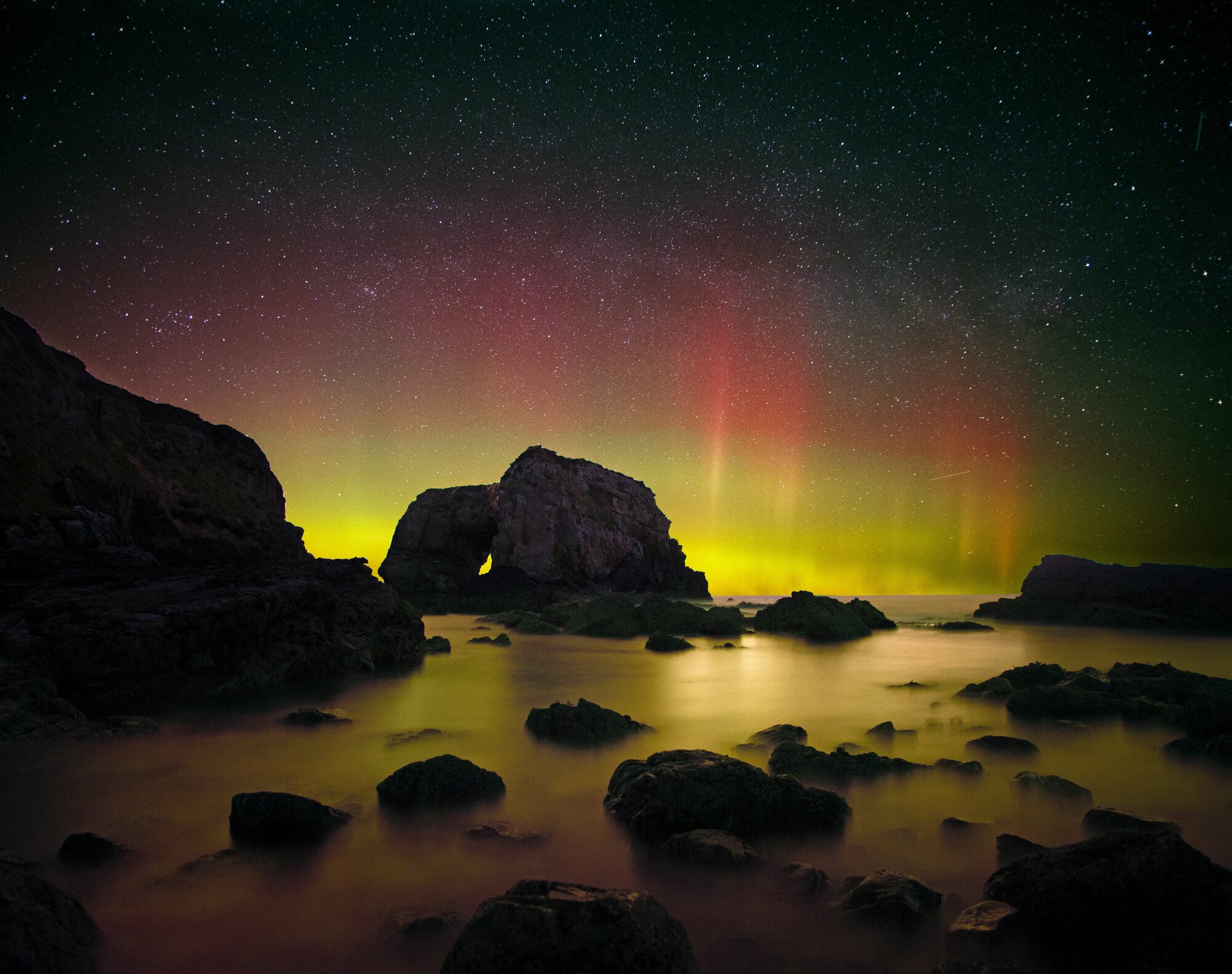 The Northern Lights glimpsed through a sea arch.