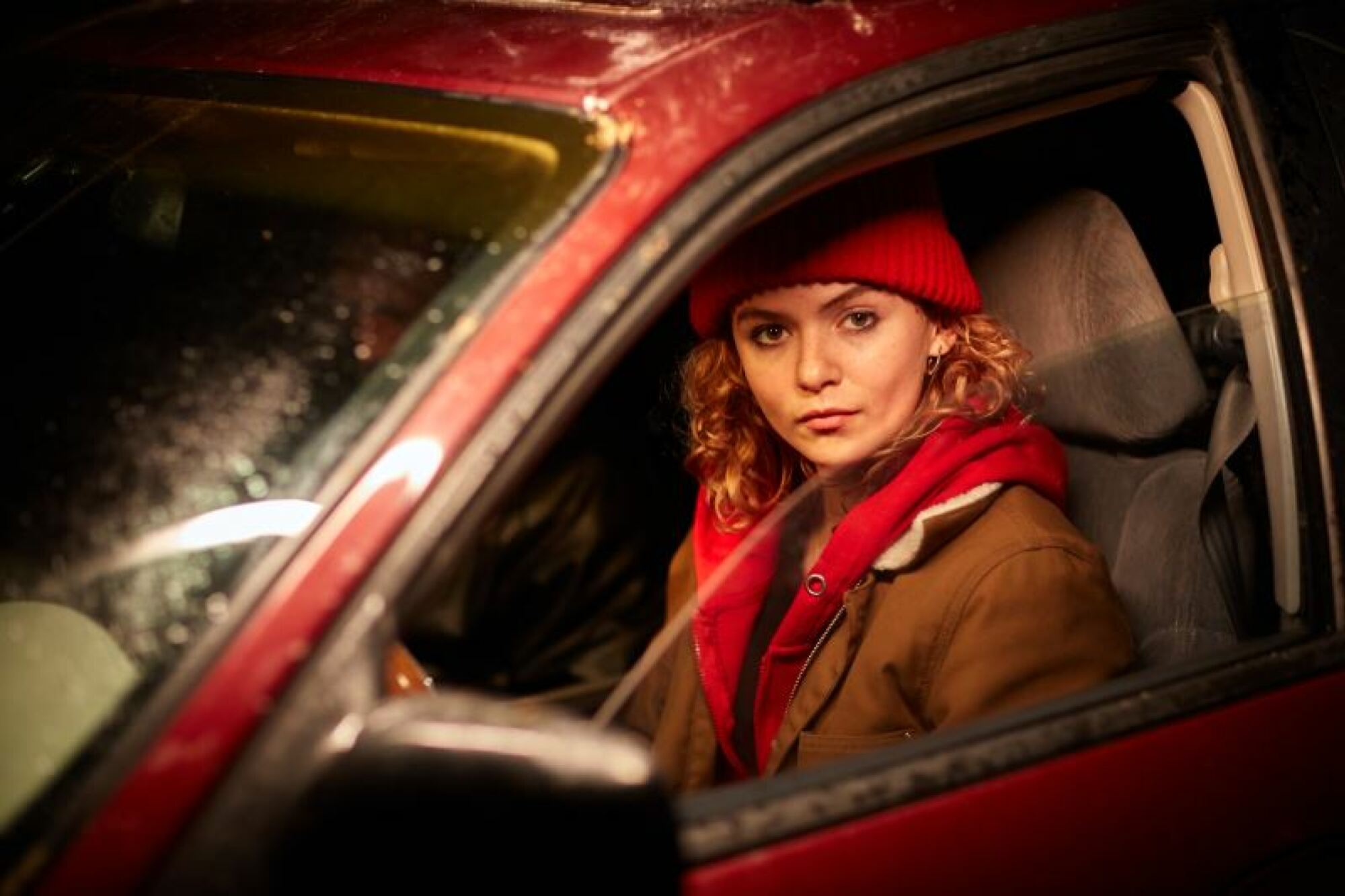 A woman in a red hat sits in a red car.