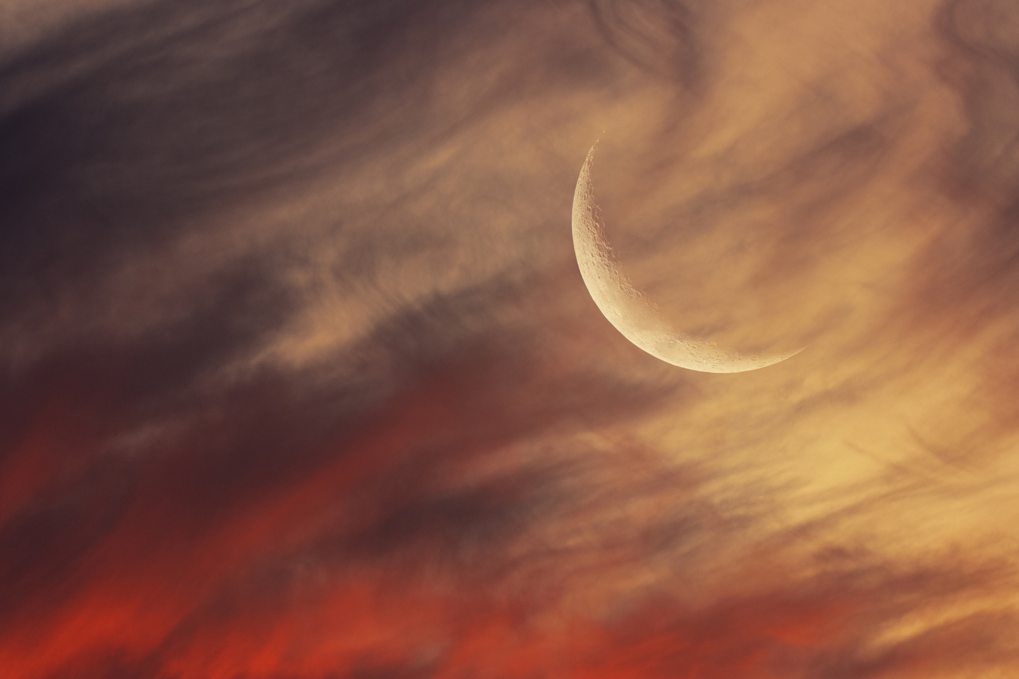 A crescent moon visible in a red and orange sky.