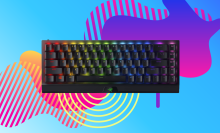 black gaming keyboard with backlit keys against a pink, yellow, and orange background