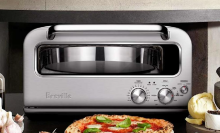 Breville pizza oven on kitchen counter with pizza in front, garlic to the left, mortar and pestle to the right