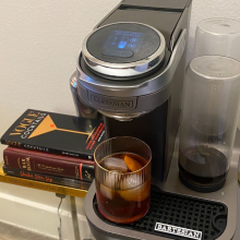 cocktail machine on glass table with a drink and recipe books 