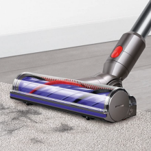 Dyson vacuum sweeping debris off a beige carpet