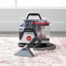Hoover carpet cleaner with red accents on pink and white rug against window with white curtain