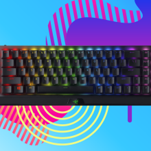 black gaming keyboard with backlit keys against a pink, yellow, and orange background