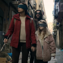 A man, woman, and child, walk on a destroyed street while wearing blindfolds. 
