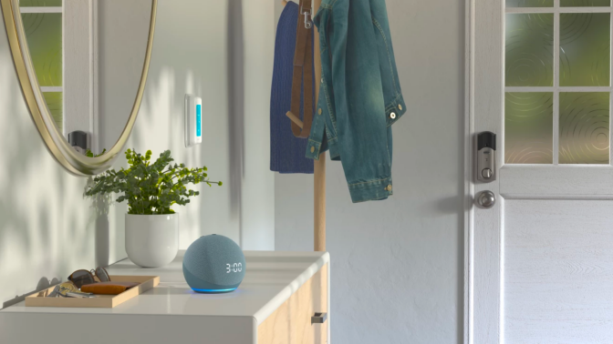 a twilight blue echo dot sitting on a white console table next to a potted plant and a wood tray filled with keys, sunglasses, and a wallet. the table is next to a door and a coat rack holding several jackets