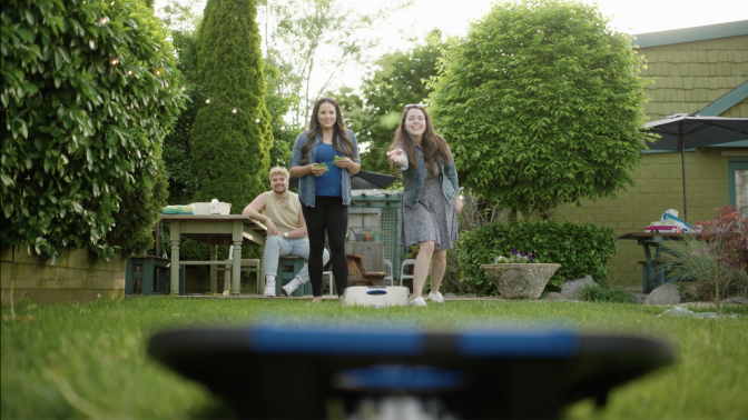Party guests play a game of beanbag toss in a backyard